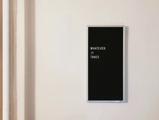 Sign on wall that spells out "whatever it takes" in white letters on a black background.