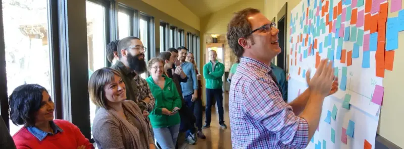 Todd Nienkerk standing at a wall of post-it notes during a team-building exercise at the Four Kitchens company retreat in 2016